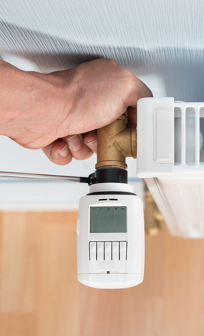 Hand eines Mechanikers, der am Regler einer Heizung schraubt